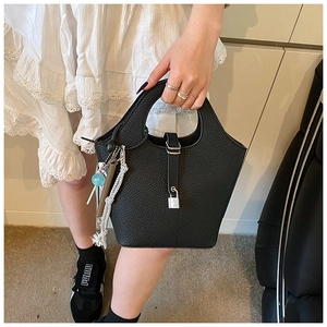 Detail of black pebbled leather bucket bag with metal lock and hanging tassel charms