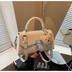 Detail of off-white crossbody bag with silver square lock and plush bear pendant accessory