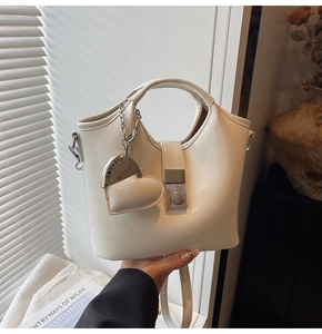 Detail of a wave-designed cream leather handbag with heart pendant and silver hardware