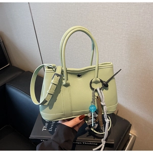 Detail der mintgrünen Eimer-Tasche aus Lychee-Leder mit Deko-Anhänger auf Sofa