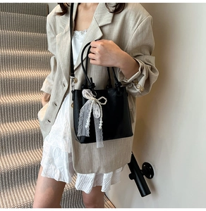 Détail du sac seau noir avec nœud en dentelle et perles porté à l'épaule