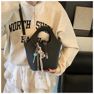 Detail of black lychee grain leather bucket bag with silver lock and trendy charms