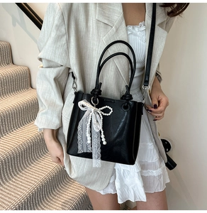 Détail du sac seau noir avec un nœud en dentelle blanche et un charmant pendentif perle