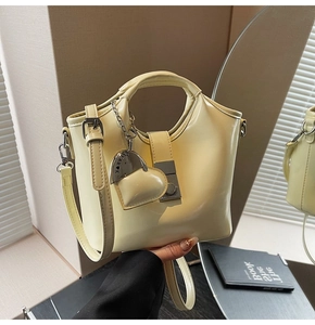 Detail of cream bucket bag with metal clasp, heart charm and adjustable shoulder strap