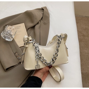 Close-up of cream glossy patent leather handbag with chunky silver chain decoration