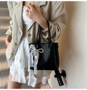 Détail du sac seau en cuir noir avec breloque délicate en perles et dentelle