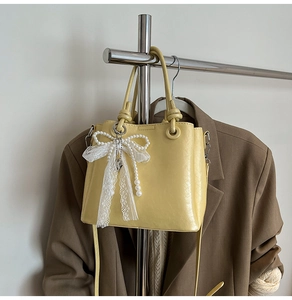 Détail du sac seau jaune clair avec nœud en dentelle et breloque en perles
