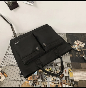 Detail of black travel bag with dual zip pockets on a metal rack in an industrial setting