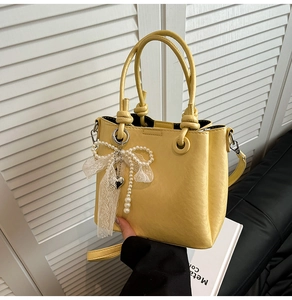Détail d'un sac seau jaune en cuir avec breloque en dentelle de perles et pendentif cœur