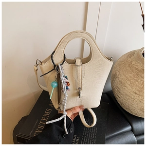 Detail of beige bucket bag with round handle and decorative charms on art books