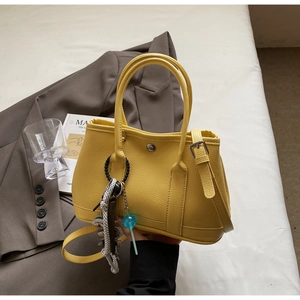 Detail der gelben Leder-Eimertasche mit Tragegriffen und dekorativem Anhänger