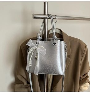 Détail du sac seau argenté métallisé avec nœud en dentelle et pendentif perle