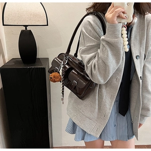Detail of dark brown glossy shoulder bag with dual front buckle pockets and plush bear charm