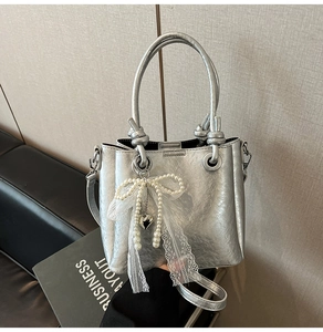 Détail du sac seau argenté avec texture cuir métallisé et nœud en dentelle et perles
