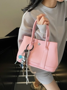 Rosafarbene Eimertasche mit Lychee-Struktur und kreativen Anhängern für den täglichen Weg