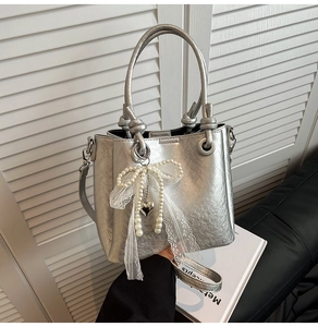 Détail du sac seau en cuir argenté avec nœud en perles, ruban dentelle et pendentif cœur