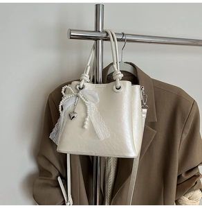 Détail du sac seau nacré avec nœud en dentelle, perles et pendentif cœur argenté