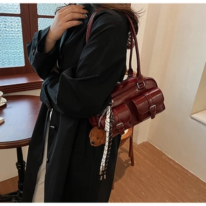Detail of burgundy glossy patent leather shoulder bag with plush bear charm and woven cord