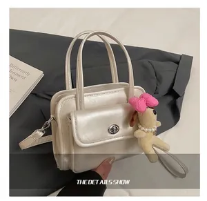 Detail of pearl beige PU leather handbag with metal turn-lock and dog charm accessory