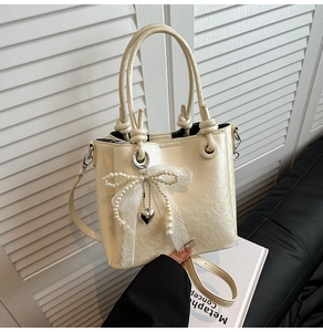 Détail du sac seau crème élégant avec nœud en dentelle de perles et pendentif cœur argenté