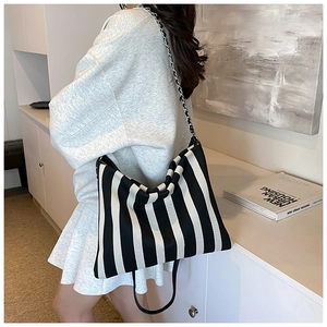 Detail of striped canvas tote bag with metal chain strap worn on model shoulder