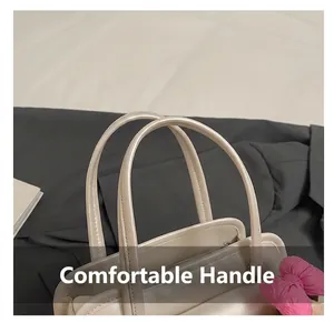Detail of cream handbag showing dual top handles and a pink bow charm accessory