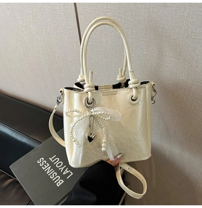 Détail du sac seau crème avec un nœud en perles et une bandoulière réglable