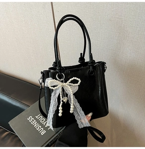 Détail du sac seau en PU noir avec un grand nœud en dentelle et perles et un cœur
