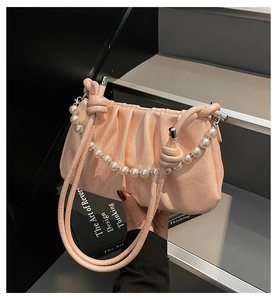 Pink pleated cloud bag with elegant pearl chain handle held in hand for scale