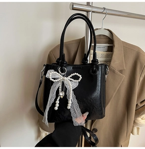 Détail du sac seau en cuir noir avec nœud en dentelle de perles et pendentif cœur