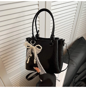 Détail du sac seau noir en cuir avec nœud en perles, ruban en dentelle et pendentif cœur
