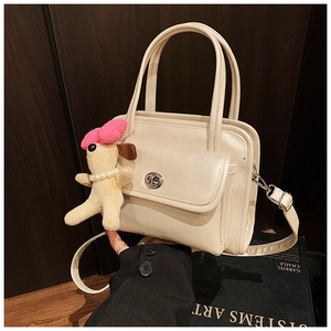 Detail of cream leather handbag featuring silver twist lock and cute plush dog charm