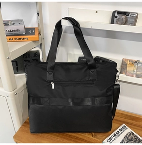 Detail of black nylon tote bag featuring reinforced leather handles and front zipper pocket