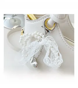Makro-Detail der weißen Ledertasche mit Perlenkette, Spitzenschleife und Herzanhänger