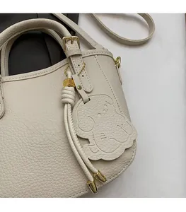 Detailed close-up of beige lychee grain leather handbag with cute dog charm and gold hardware