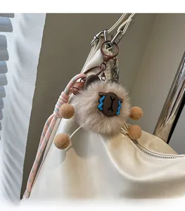 Dettaglio di un ciondolo in peluche marrone con simboli a croce blu appeso a una borsa bianca