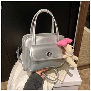 Detail of silver patent leather handbag featuring a metal turn-lock and cute puppy charm