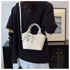 Detail der cremeweißen Handtasche mit Spitzenschleife, Perlenkette und Herzanhänger