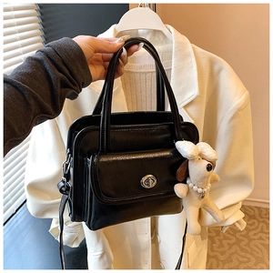Detail of black glossy handbag with silver twist lock and cute white plush puppy charm
