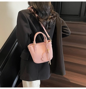 Pink lychee texture bucket bag with cat charm and adjustable strap shown on model