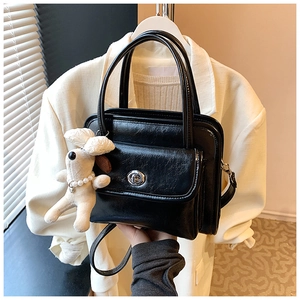 Detail of black box bag with oil-wax texture, silver metal lock and plush puppy charm