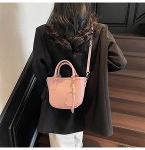 Pink lychee grain leather bucket bag with dog charm shown worn on models shoulder