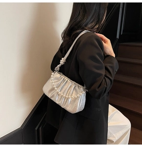 Detail of silver pleated cloud bag with pearl chain decoration on a model shoulder