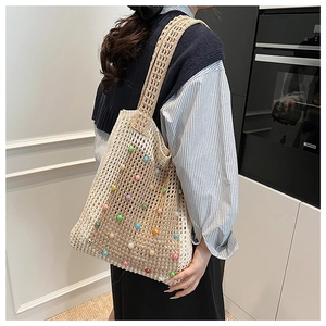 Detail of beige crochet hollow tote bag with colorful beads worn on the shoulder