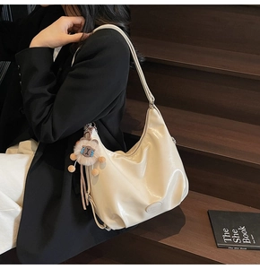 Dettaglio borsa hobo beige con ciondolo a forma di orso su sfondo di legno