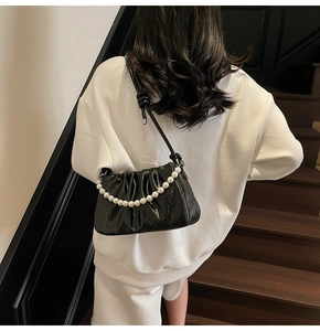 Detail of a black ruched cloud bag with pearl chain and knotted shoulder strap on a model