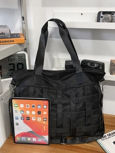 Large black nylon tote bag with quilted texture and adjustable strap next to an iPad