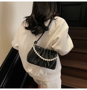 Detail of black pleated cloud bag with elegant pearl chain and knotted leather strap