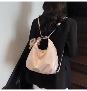 Dettaglio borsa pendolare in pelle lucida rosa chiaro con pompon e targhetta in metallo