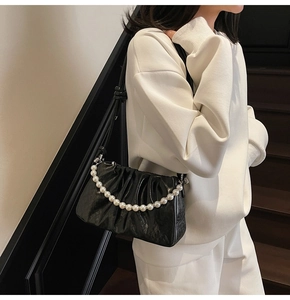 Detailed view of black pleated cloud bag with elegant pearl chain on a stylish crossbody